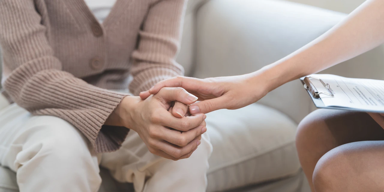 A therapist holds a client’s hand during a mental health support session, reflecting compassion, trust and emotional guidance throughout recovery.