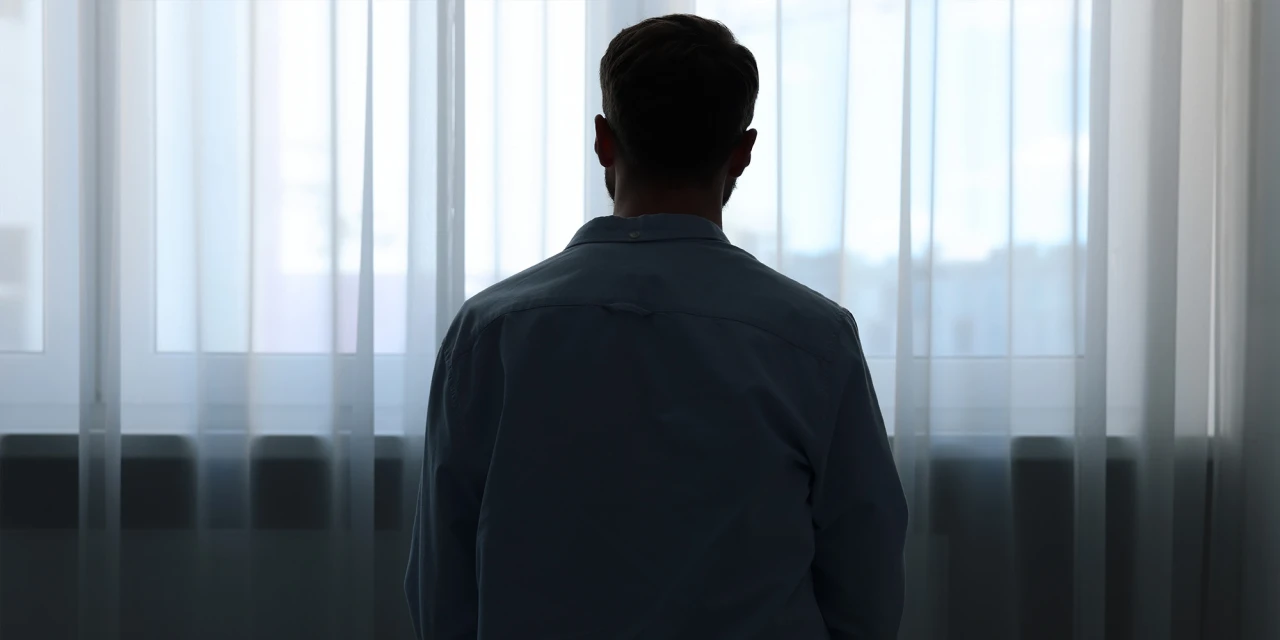 A man sits alone in front of a window in silence, showing feelings of isolation, emotional numbness and depression.