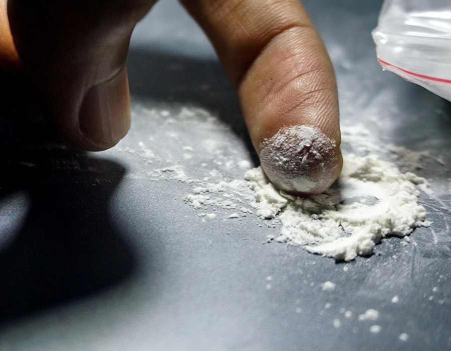 Close-up of a finger touching a pile of white cocaine powder.