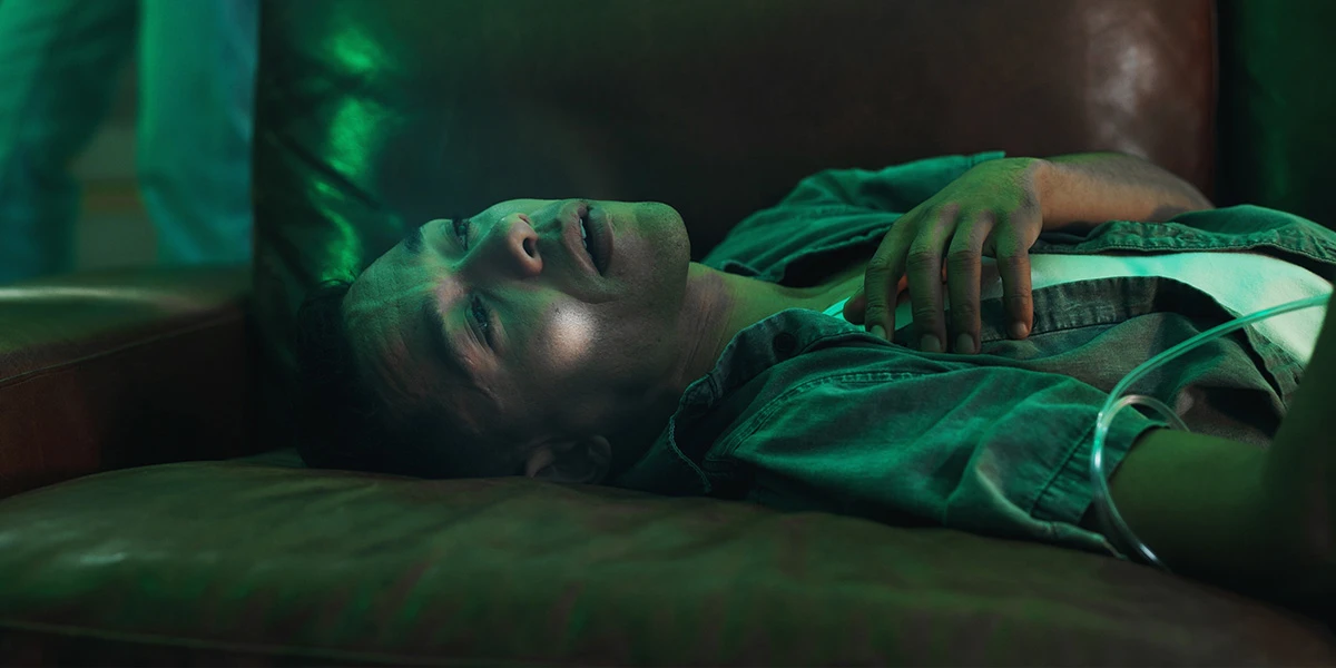 Unresponsive young man lying on a leather sofa in green light, illustrating fentanyl overdose