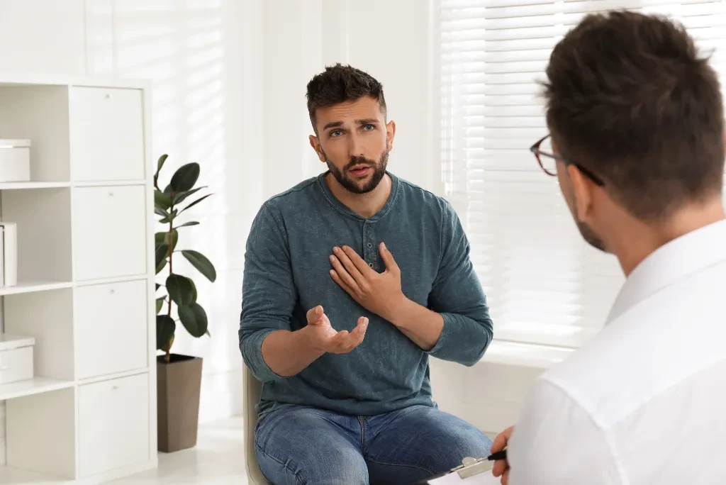 Two men in conversation in a therapy room, one acting as the doctor and the other as the client, who appears concerned.