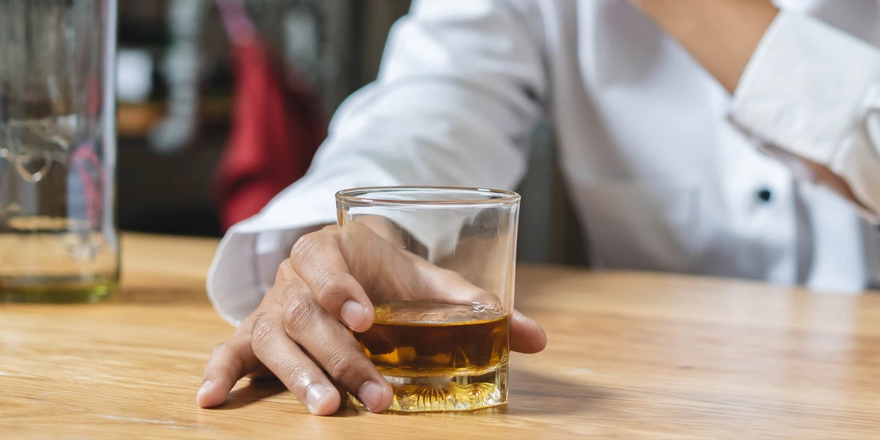 A person reaches for a glass of whiskey while sitting in emotional distress, showing the impact alcohol addiction can have on your mental wellbeing.