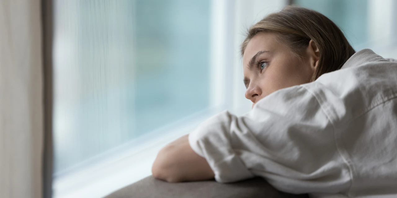 A woman sits curled up on a sofa with her head resting on her arms, reflecting sadness, exhaustion and the emotional weight of depression.