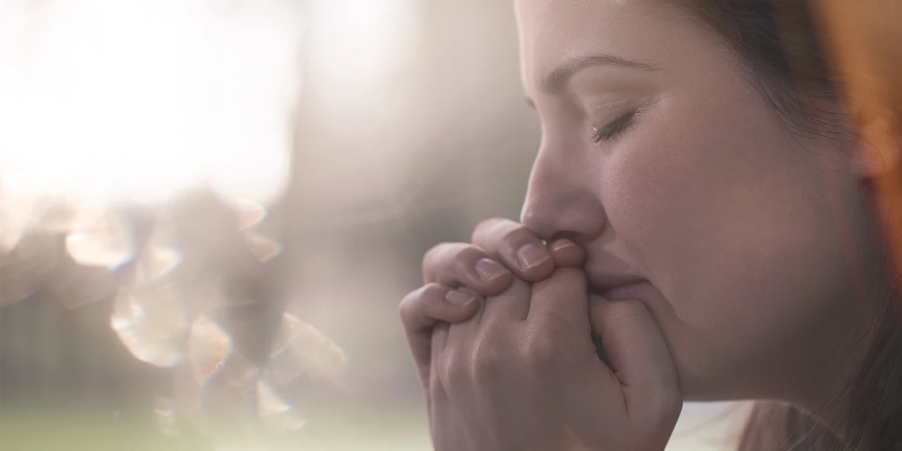A woman sits with her hands near her face in emotional distress, reflecting the anxiety, fear and emotional impact trauma can have on your daily life.