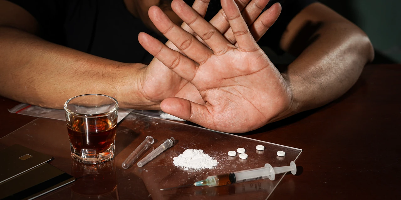 A person holds up their hands beside white powder, pills, alcohol and syringes, symbolising the decision to seek help for heroin addiction.