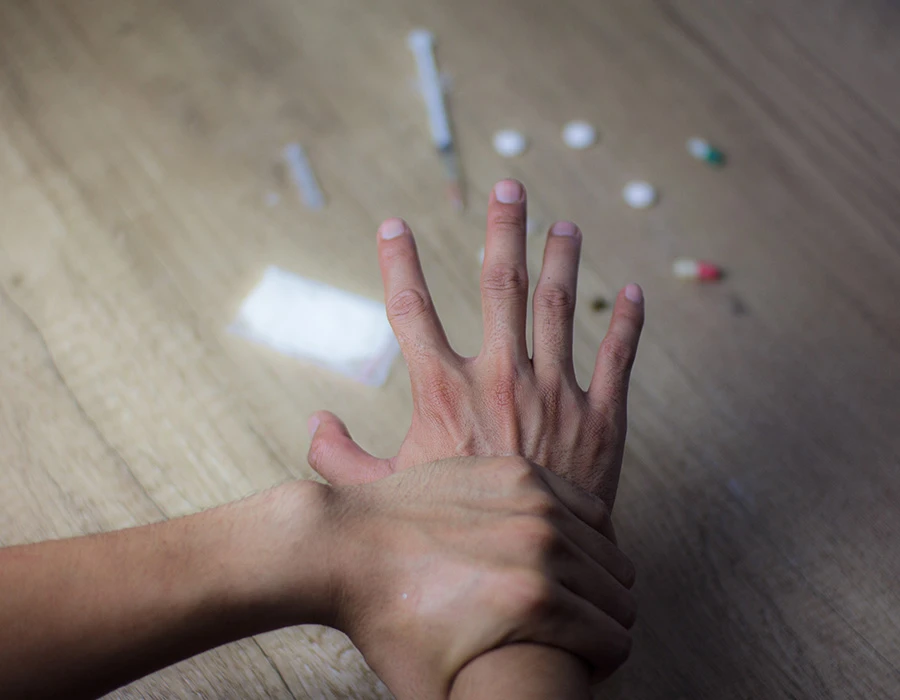 Hand held back by the other hand from drugs on a table, illustrating ketamine addiction treatment