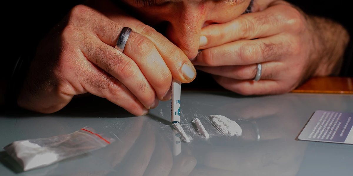 Man snorting a line of cocaine through a rolled banknote, illustrating cocaine nose damage.