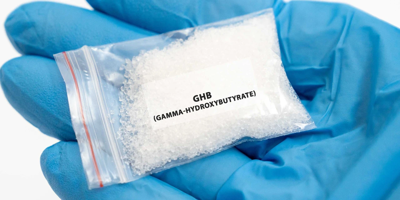 A gloved hand holds a small bag labelled GHB, showing a substance associated with GHB addiction and the dangers of recreational drug use.