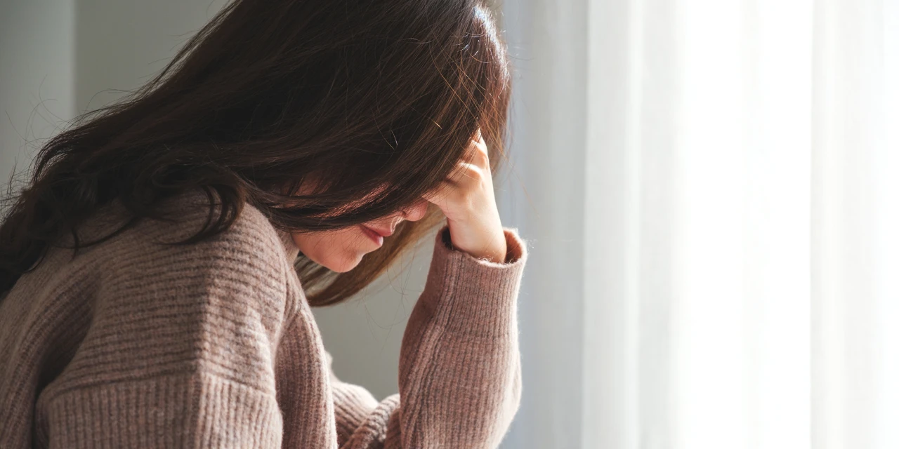 A woman sits by the window in silence, reflecting feelings of anxiety, emotional exhaustion and mental strain during a difficult period.
