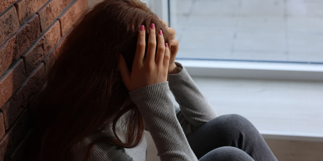 Een jongere zit alleen tegen een muur, met het hoofd in de handen, wat de emotionele last en eenzaamheid weerspiegelt die gepaard gaan met gedragsverslaving.