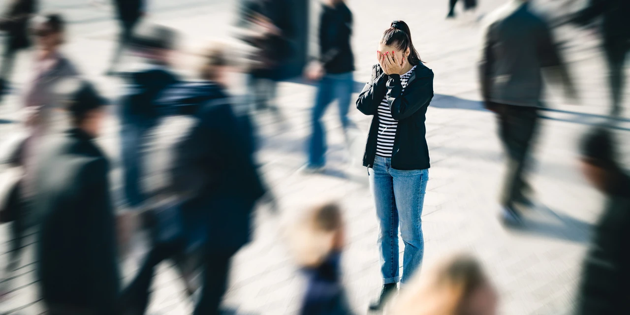 A woman stands in a crowded public space while feeling overwhelmed by anxiety, stress and emotional pressure from her surroundings.