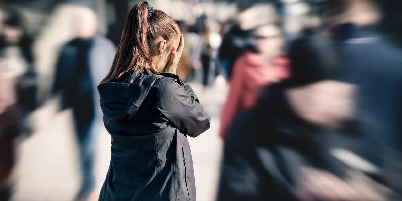 A woman stands in a busy street with blurred people moving around her, reflecting overwhelm, fear and the intense feelings linked to panic attacks.