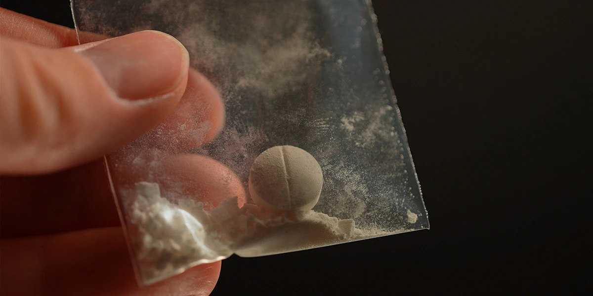 Scored white tablet and loose powder in a small plastic bag, illustrating codeine addiction