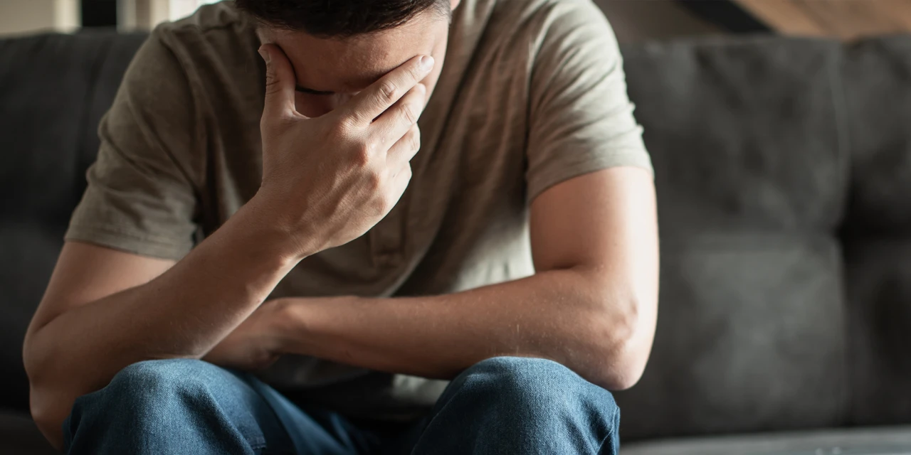 A man sits alone covering his face, illustrating the emotional exhaustion, anxiety and isolation linked to behavioural addiction.