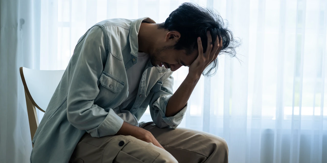A man sits alone with his head in his hand, showing emotional distress and exhaustion related to anxiety and overwhelming thoughts.