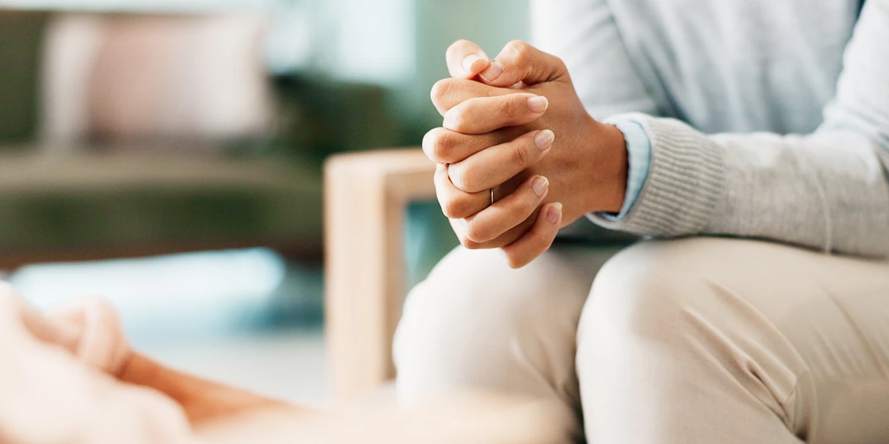 A close-up of a person sitting with their hands folded together in a calm, attentive manner during a conversation.