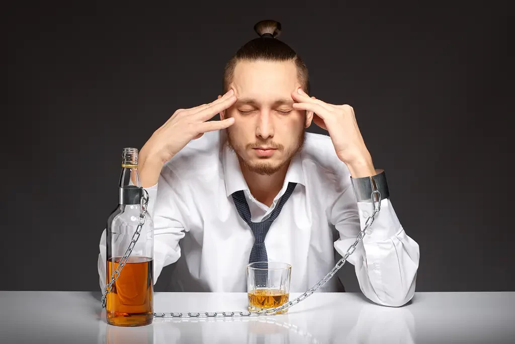 A man holding his head in his hands, looking concerned and chained to a bottle of liquor.