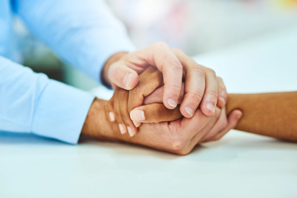 Two people holding hands in a comforting way, with a blurry, light background.