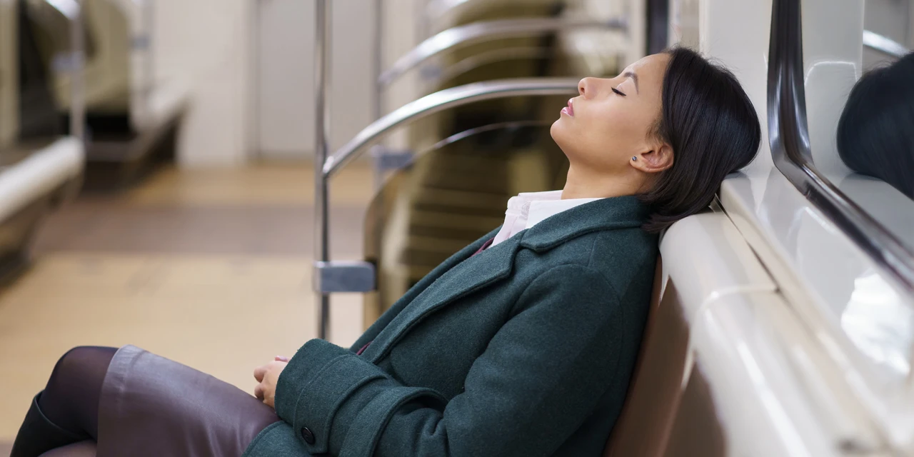 A woman sits alone with her eyes closed, showing the physical and emotional exhaustion often experienced during burn out and chronic stress.