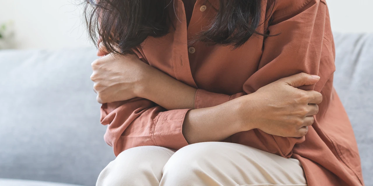 A woman sits with her arms wrapped around herself, reflecting emotional distress, anxiety and the isolating impact PTSD can have on daily life.
