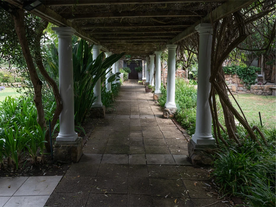 Rehab centre garden, with a gallery of white columns surrounded with green and covered with a wooden ceiling. 