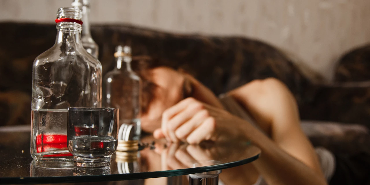 Wat is alcoholvergiftiging? Een persoon ligt bewusteloos naast flessen en een glas.