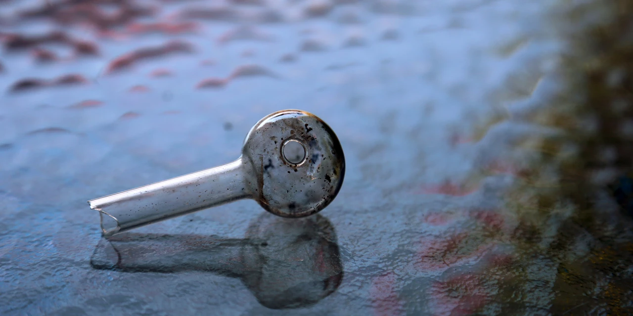 A used glass pipe lies on a reflective surface, showing drug paraphernalia commonly associated with crystal meth addiction.