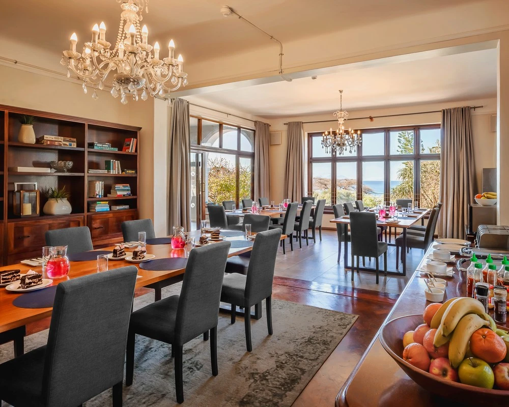 A formal dining room with chandeliers and sea views through large windows.