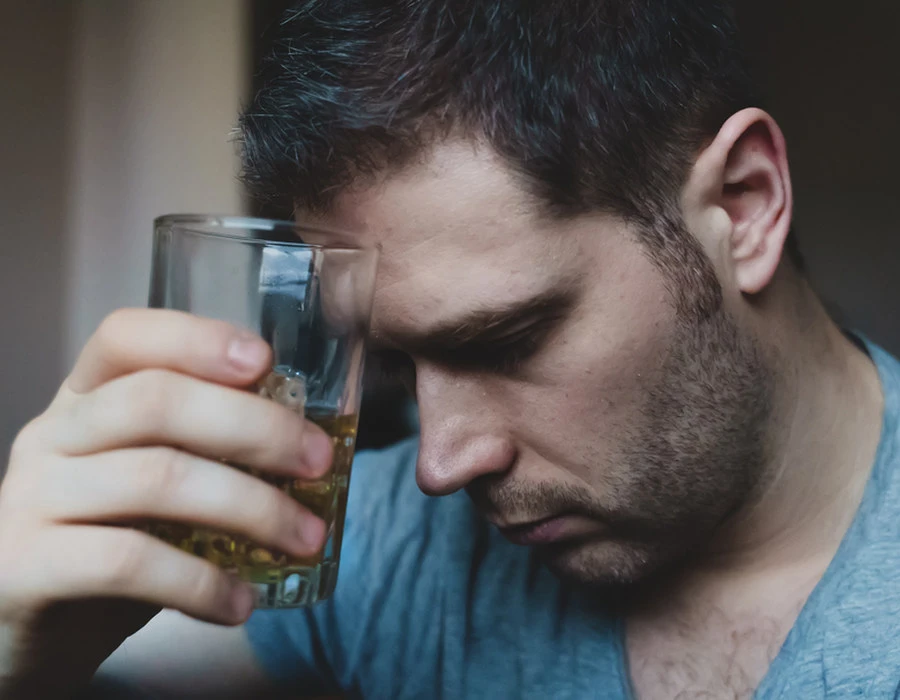 A man with his head bowed holds a glass of whisky to his forehead. Alcohol as a form of self-medication for ADHD.
