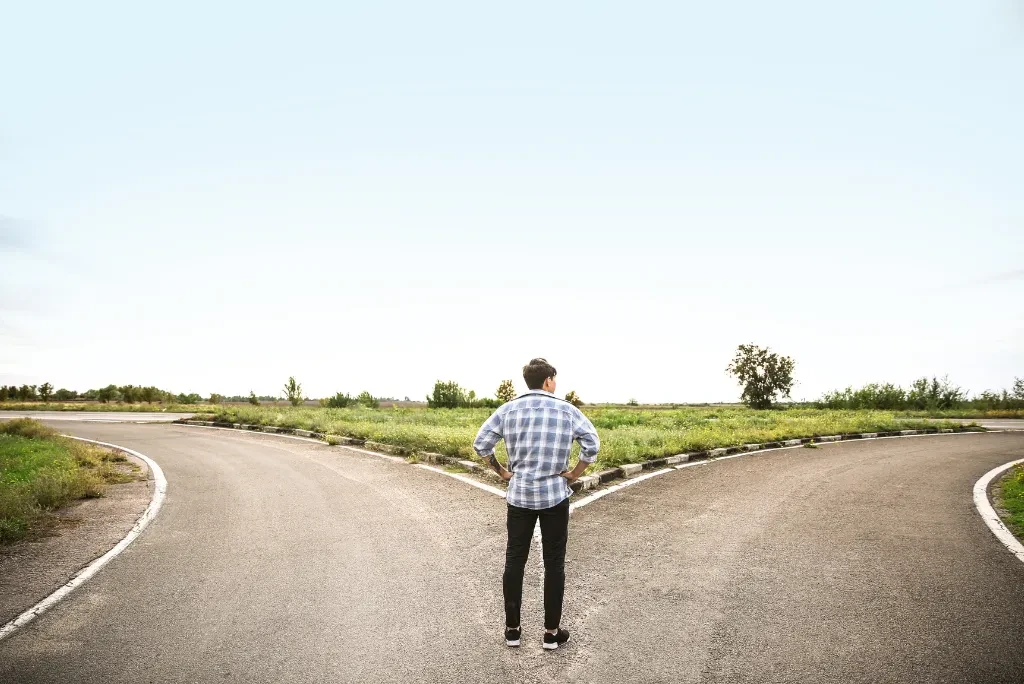 A person in a checkered shirt standing at a cross roads, contemplating which way to go.