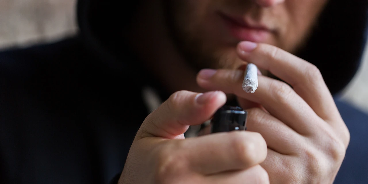 A person lights a marijuana joint with a lighter, illustrating recreational cannabis use and behaviours associated with marijuana addiction.