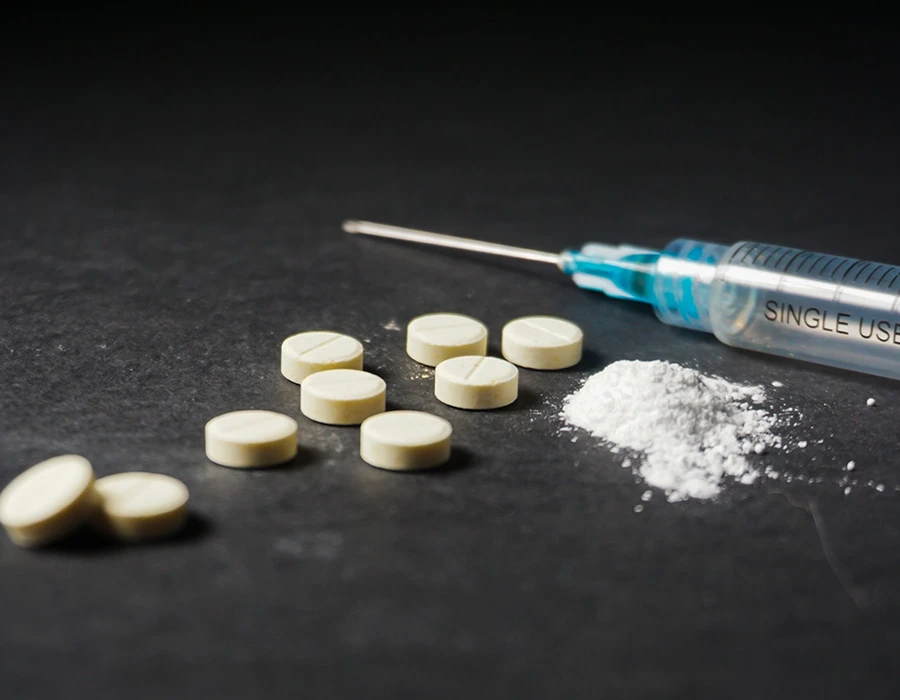 Syringe, white powder and tablets on a dark surface, illustrating heroin overdose risk
