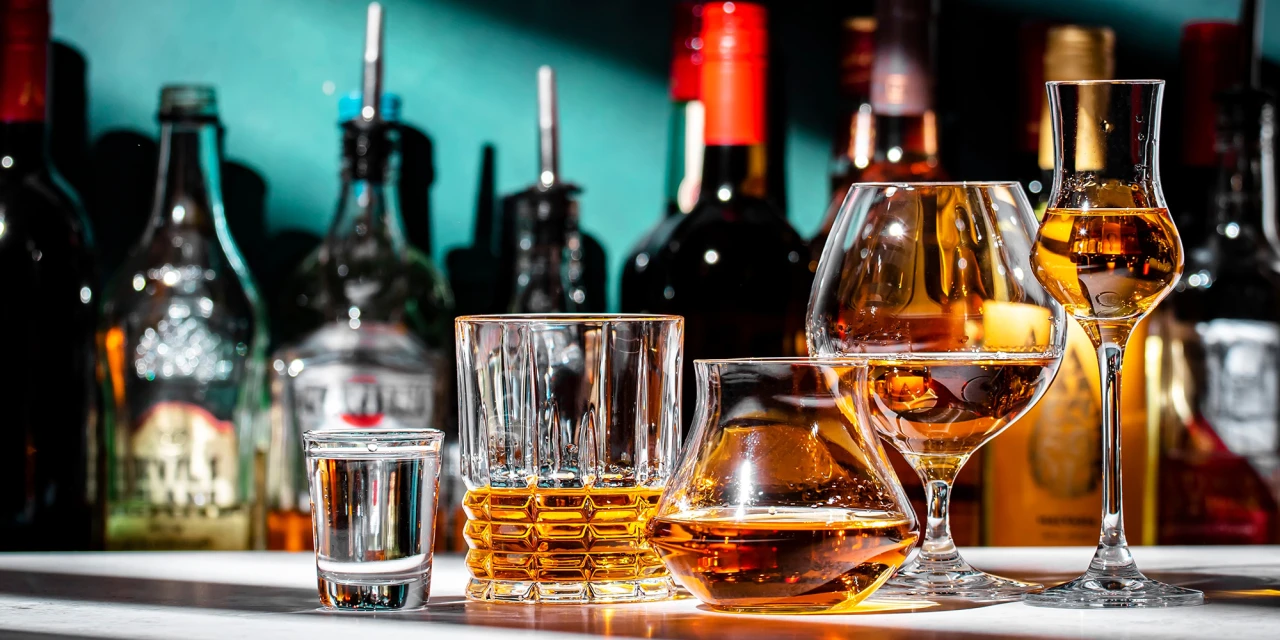 Verschillende glazen met sterke drank en flessen op een bar.
